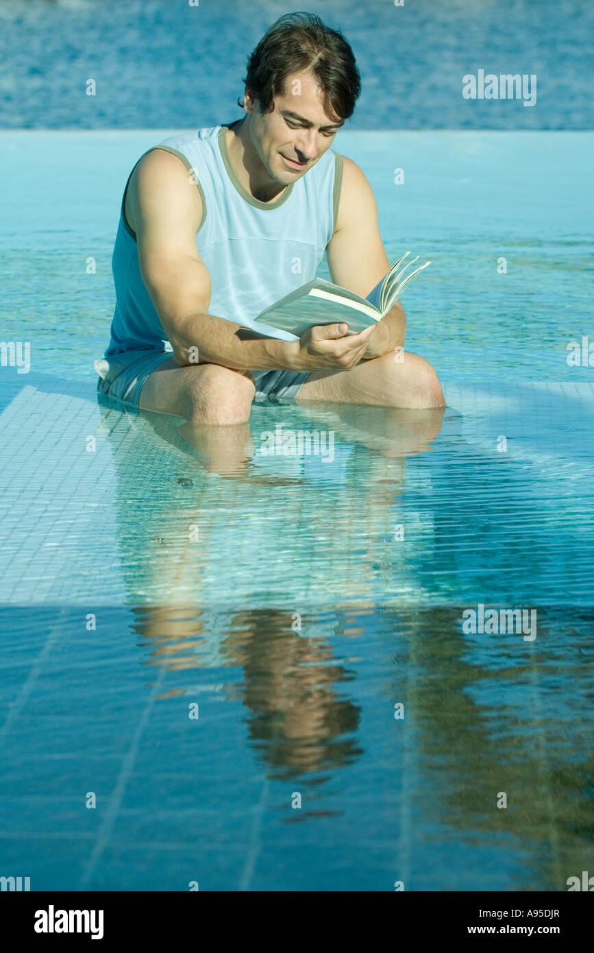 Uomo seduto in piscina, la lettura Foto Stock