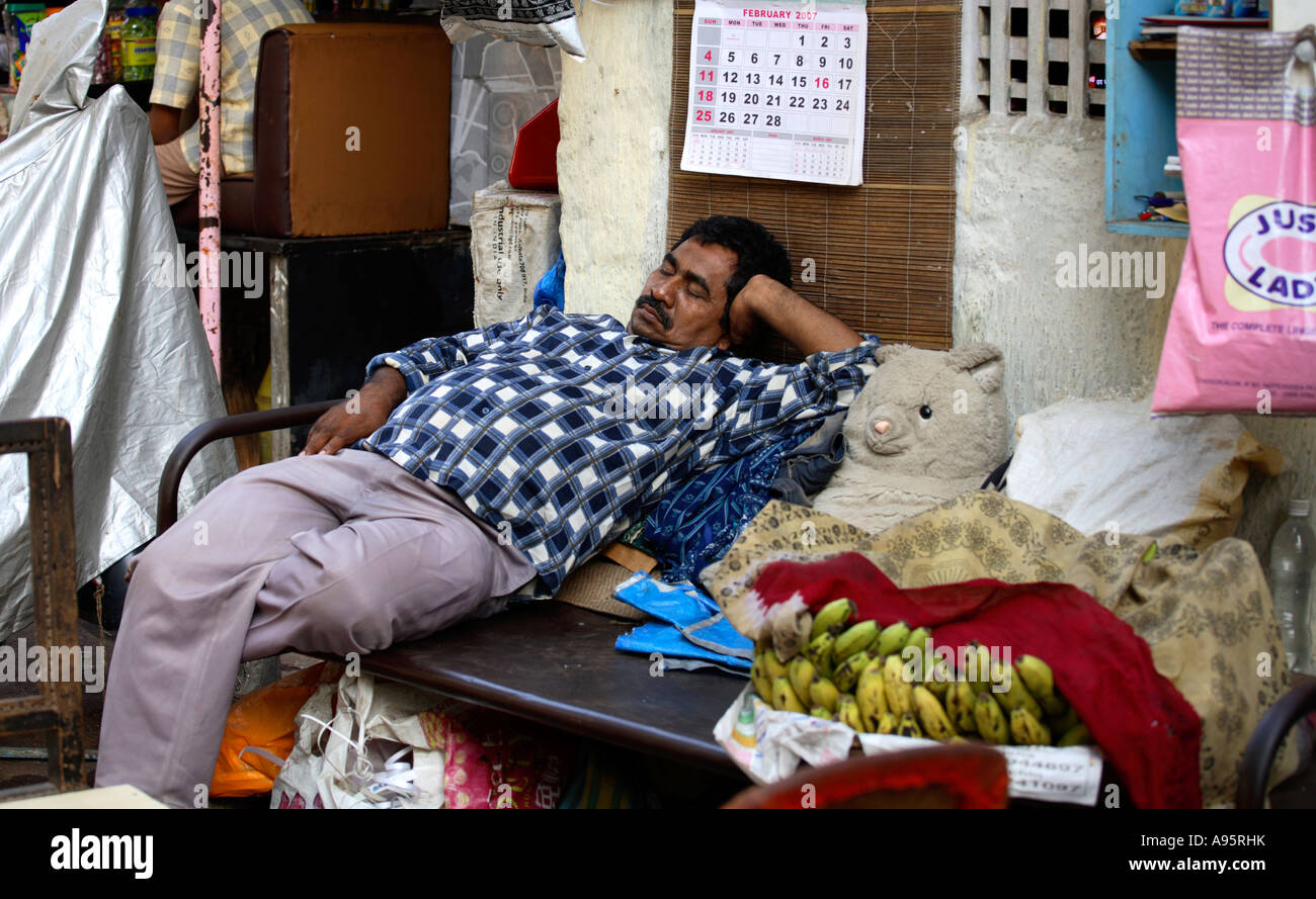 L'uomo indiano rilassa il negozio all'aperto sulla strada, Mumbai, India Foto Stock