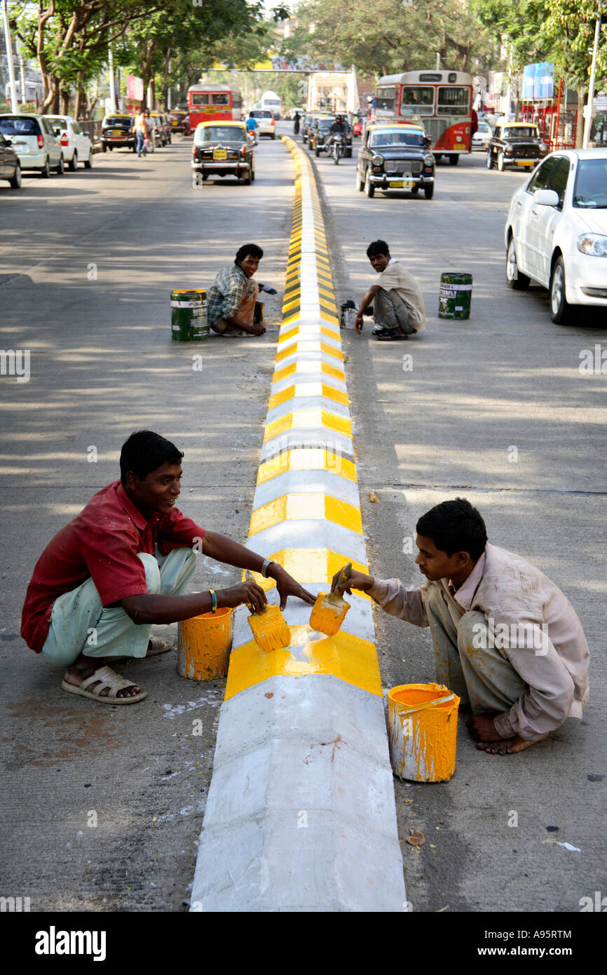 Giovani ragazzi indiani dipingono i cartelli stradali con vernice gialla e nera sul separatore di corsia, Mumbai, India Foto Stock