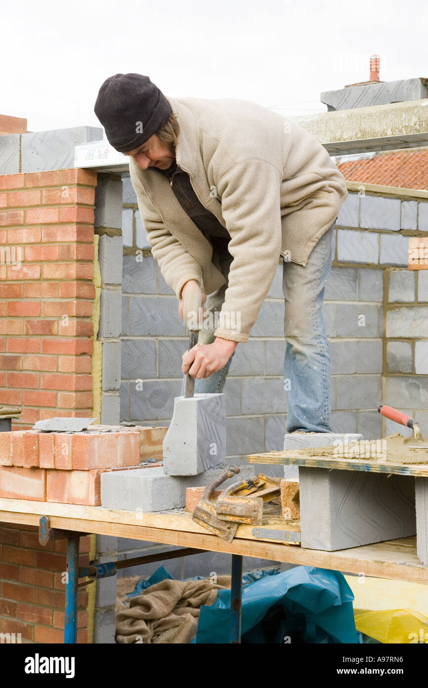 Un muratore utilizzando un piastrone scalpello per ^tagliare blocchi di costruzione Foto Stock