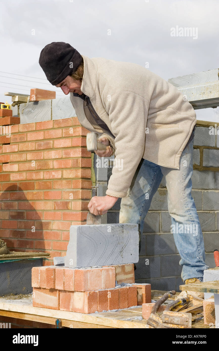 Un muratore utilizzando un piastrone scalpello per ^tagliare blocchi di costruzione Foto Stock