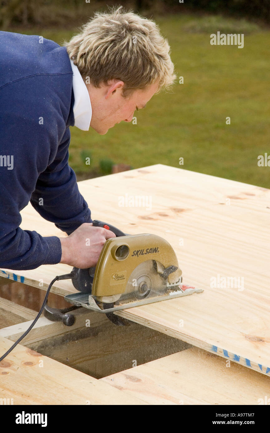 Un falegname utilizzando una sega circolare elettrica per il taglio di un foglio di legno compensato Foto Stock