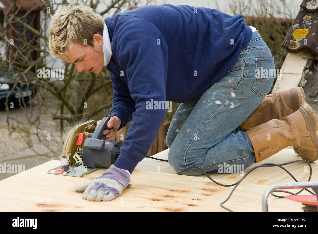 Un falegname utilizzando una sega circolare elettrica per il taglio di un foglio di legno per la costruzione di un tetto Foto Stock