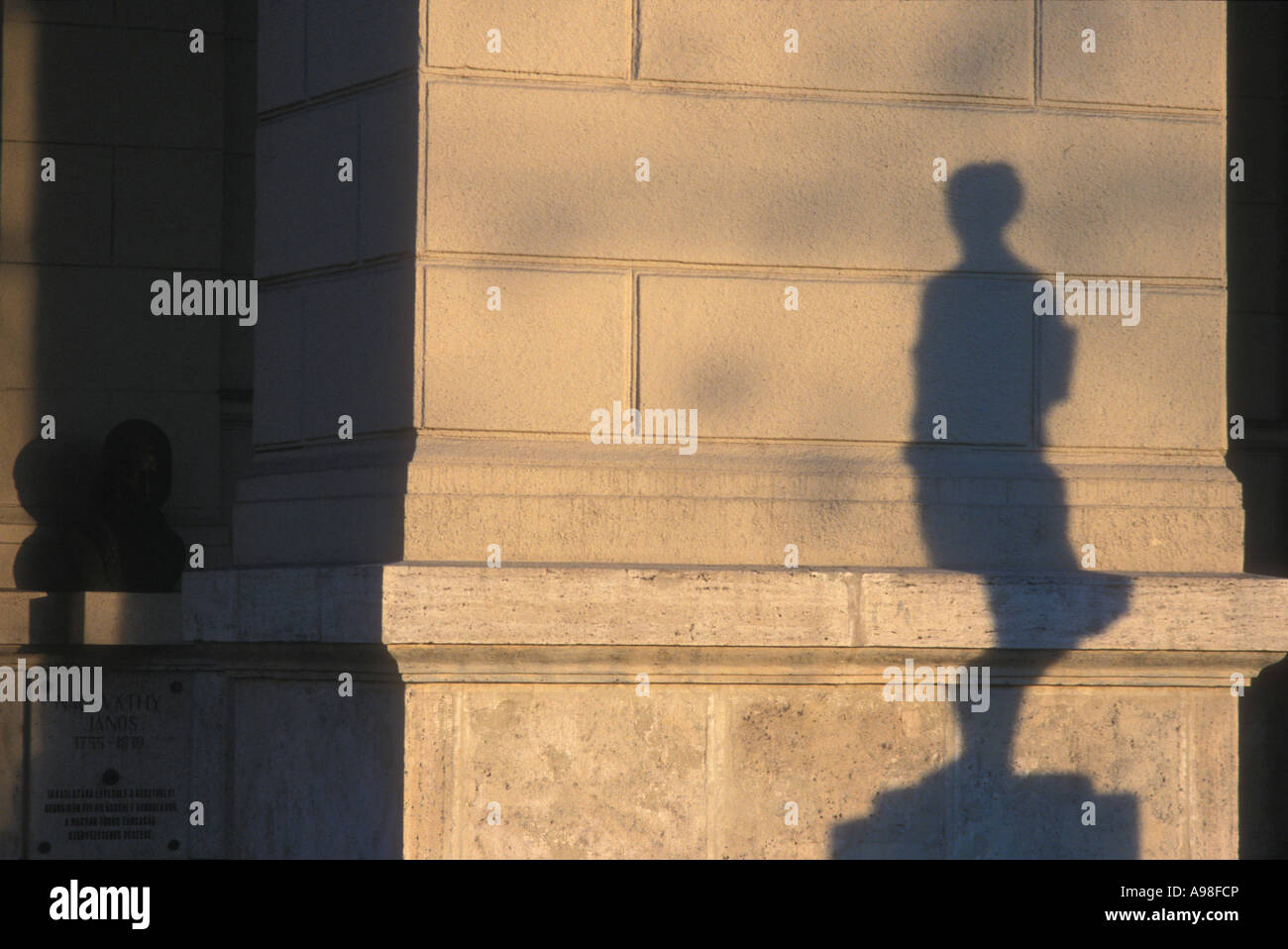 L ombra di una statua è colato su di una parete di frastagliate mentre un'altra statua, in ombre, guarda a. Nel tardo pomeriggio la luce in Budapest. Foto Stock