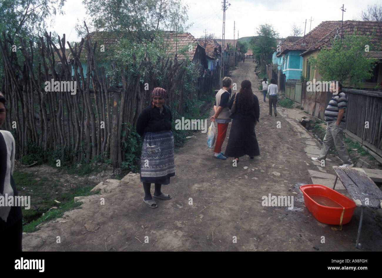 Popolazione zingara, molti in abiti etnici, camminare lungo fangoso strada principale del loro villaggio rumeno. Foto Stock