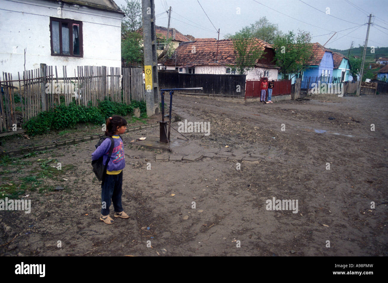 Sezione di zingaro del villaggio rumeno di Soard che mostra la strada sterrata e piccole case di livello. Una piccola ragazza è in attesa. Foto Stock