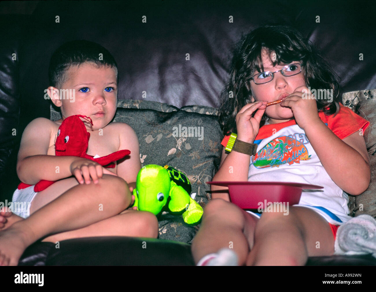 I bambini a guardare il film spaventoso in TV mentre mangia e con giocattoli Foto Stock