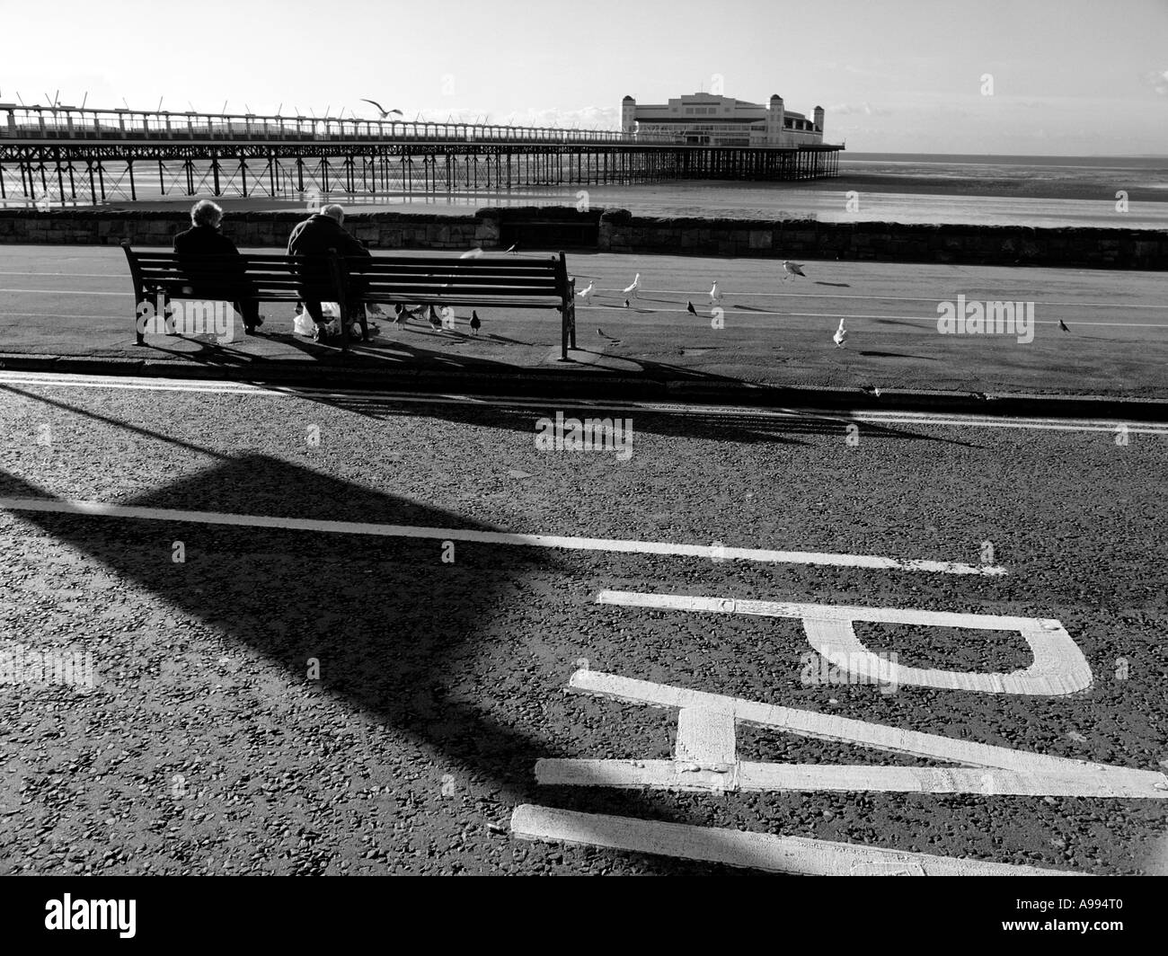 Vecchia coppia su un banco di lavoro presso il lungomare di Weston-Super-Mare, Somerset, Inghilterra. (Immagine in bianco e nero) Foto Stock