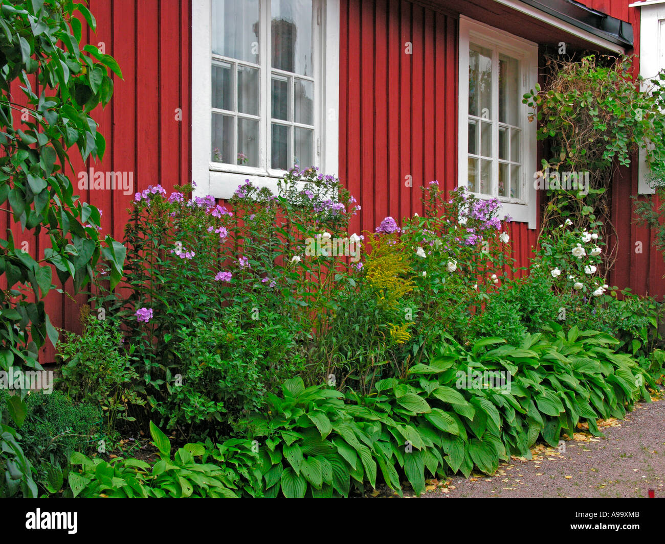 Tes skandinavisches Holzhaus mit Blumenrabatt davor red skandinavian Timber house timberhouse con letto di fiori Foto Stock