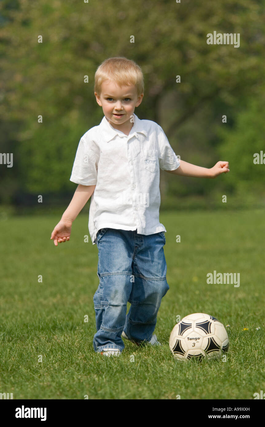 Un giovane ragazzo biondo giocando a calcio nel parco su una soleggiata giornata di primavera. Foto Stock