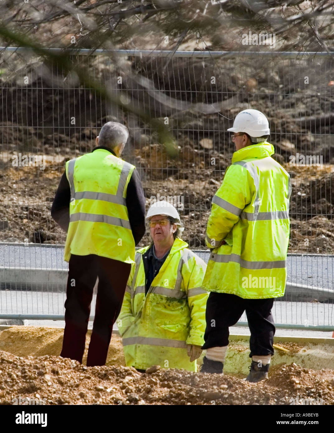 Un gruppo di operai che indossa giallo riflettente cappotti e bianco duro cappelli. Responsabile del sito. Sito di costruzione nel Regno Unito. Foto Stock
