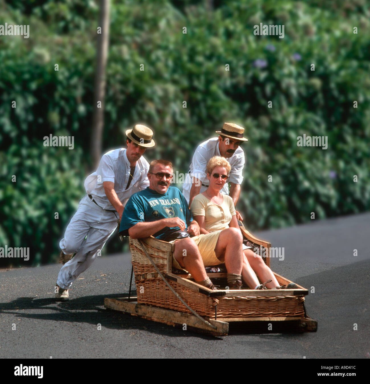Coppia di mezza età che viene spinto in una pista da slittino tradizionale tra monte e Funchal, Madeira, Portogallo Foto Stock