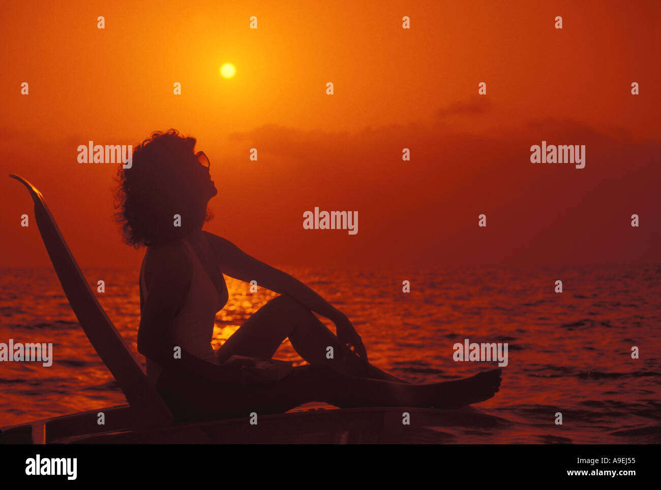 Spiaggia tropicale silhouette donna sulla poltrona guardando il sole cielo arancione drammatico Foto Stock