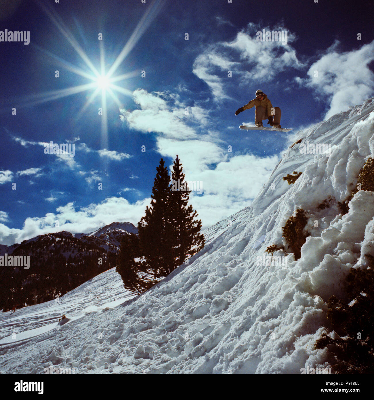 Snowboarder snowboard off roccia edge tramite l'aria cieli blu e nuvole Foto Stock