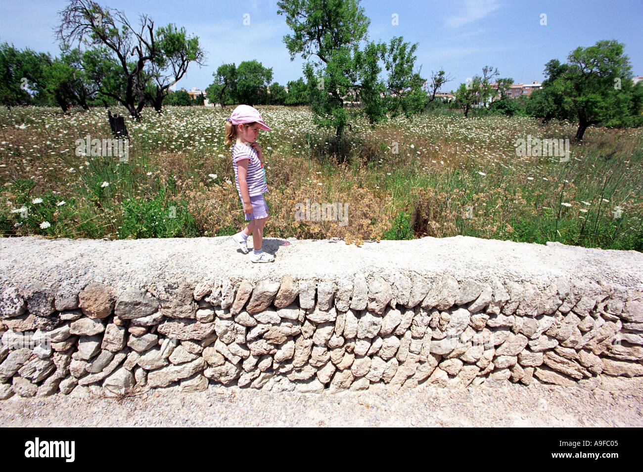 Una ragazza cammina lungo un muro con le rovine Romane sito in Alcudia Maiorca Foto Stock