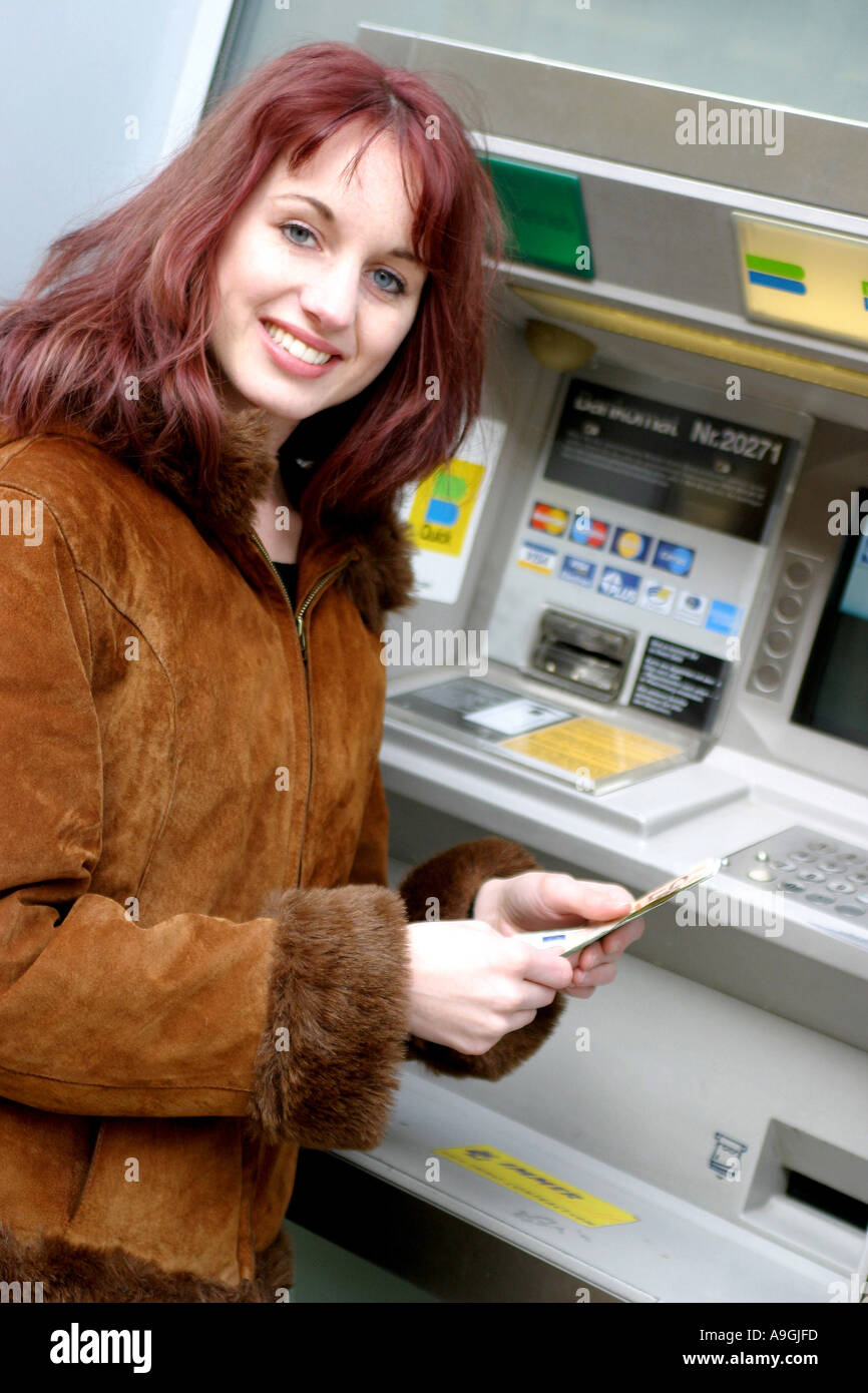 I capelli rossi donna su automatic teller machine, tenendo le banconote in una mano. Foto Stock