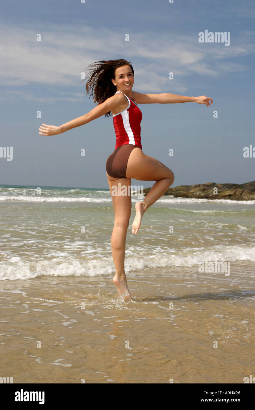 Donna salto sulla spiaggia, indossando t-shirt rossa e pantaloncini. Foto Stock