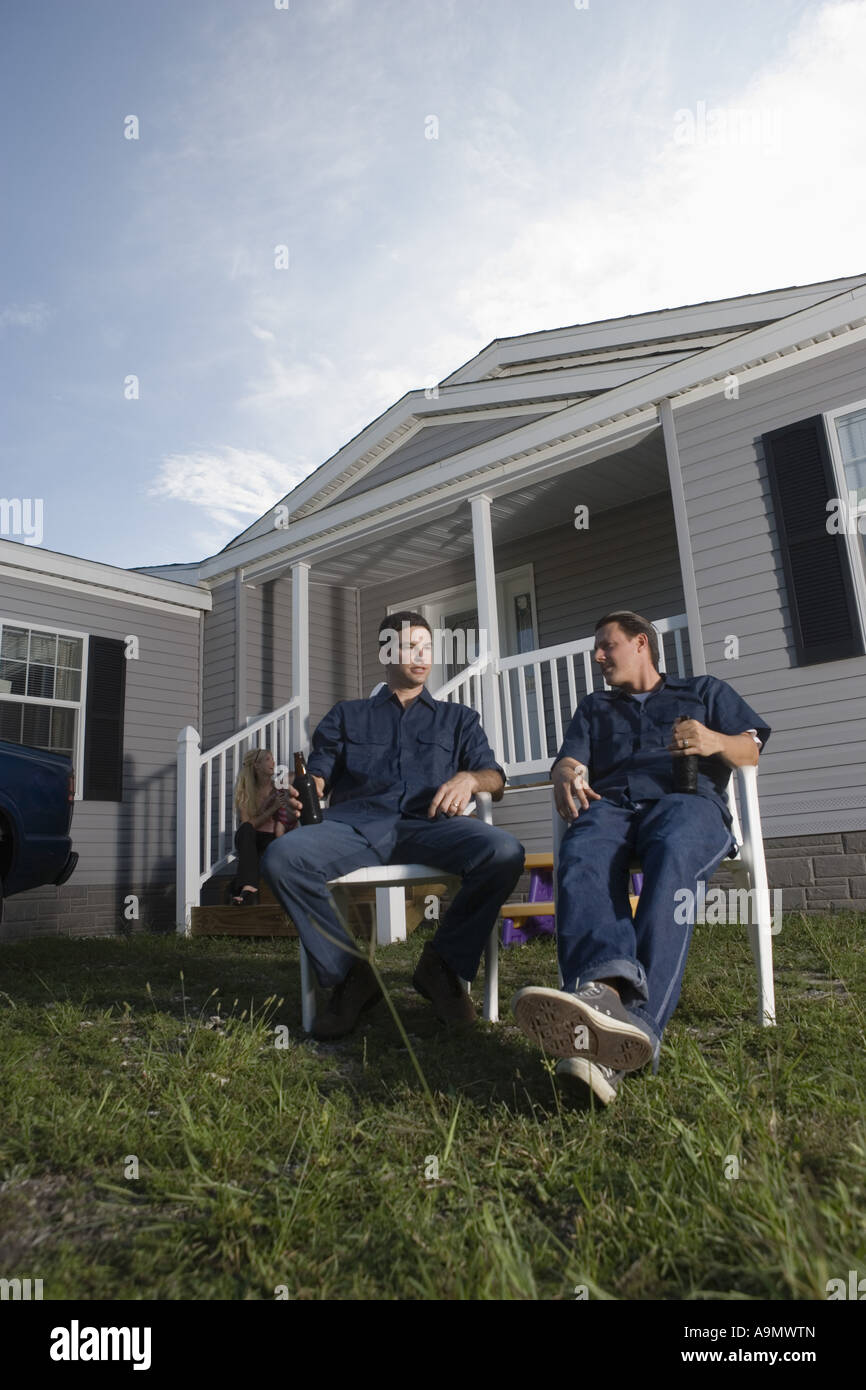 Colletto blu uomini seduti e tenendo le bottiglie di bevande in cortile anteriore del rimorchio home Foto Stock