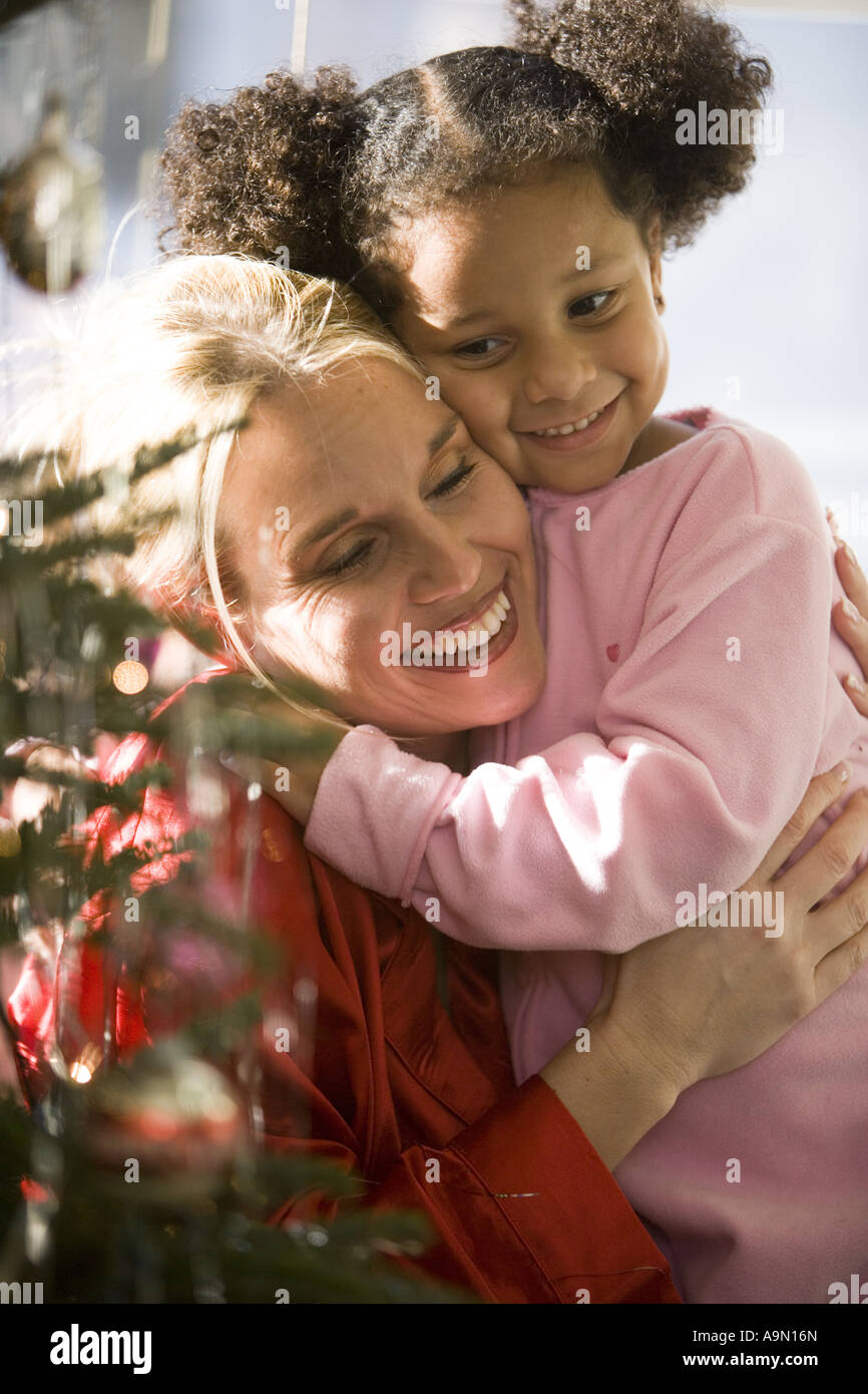 Madre e figlia in pigiama abbracciando il prossimo per albero di Natale Foto Stock