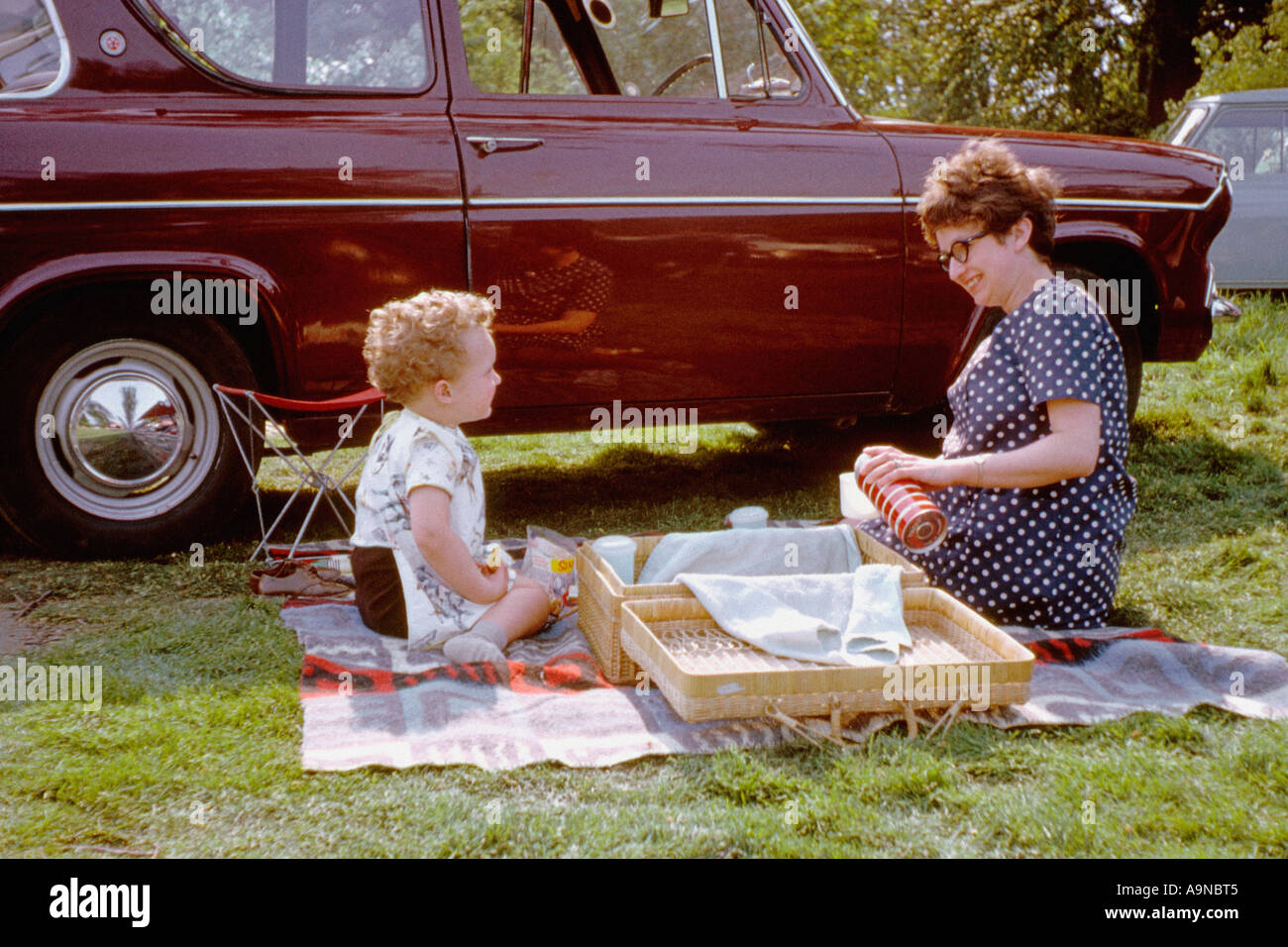Un bambino piccolo e una giovane donna seduti su una coperta da picnic con un cestino di vimini. REGNO UNITO. Intorno agli anni '1960 Foto Stock