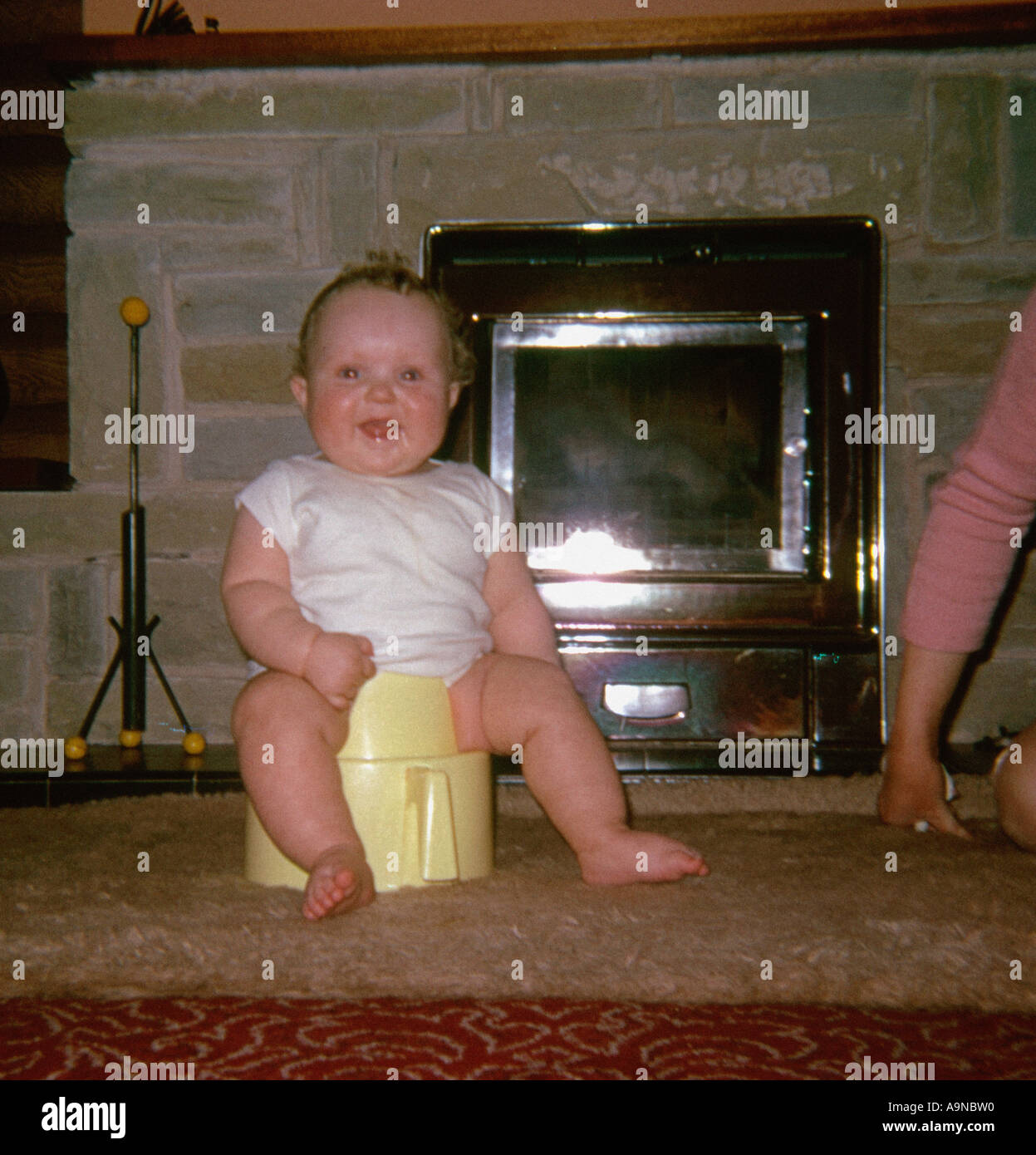 Sorridente bambino seduto su un vasino di fronte al fuoco intorno agli anni '1960 Foto Stock