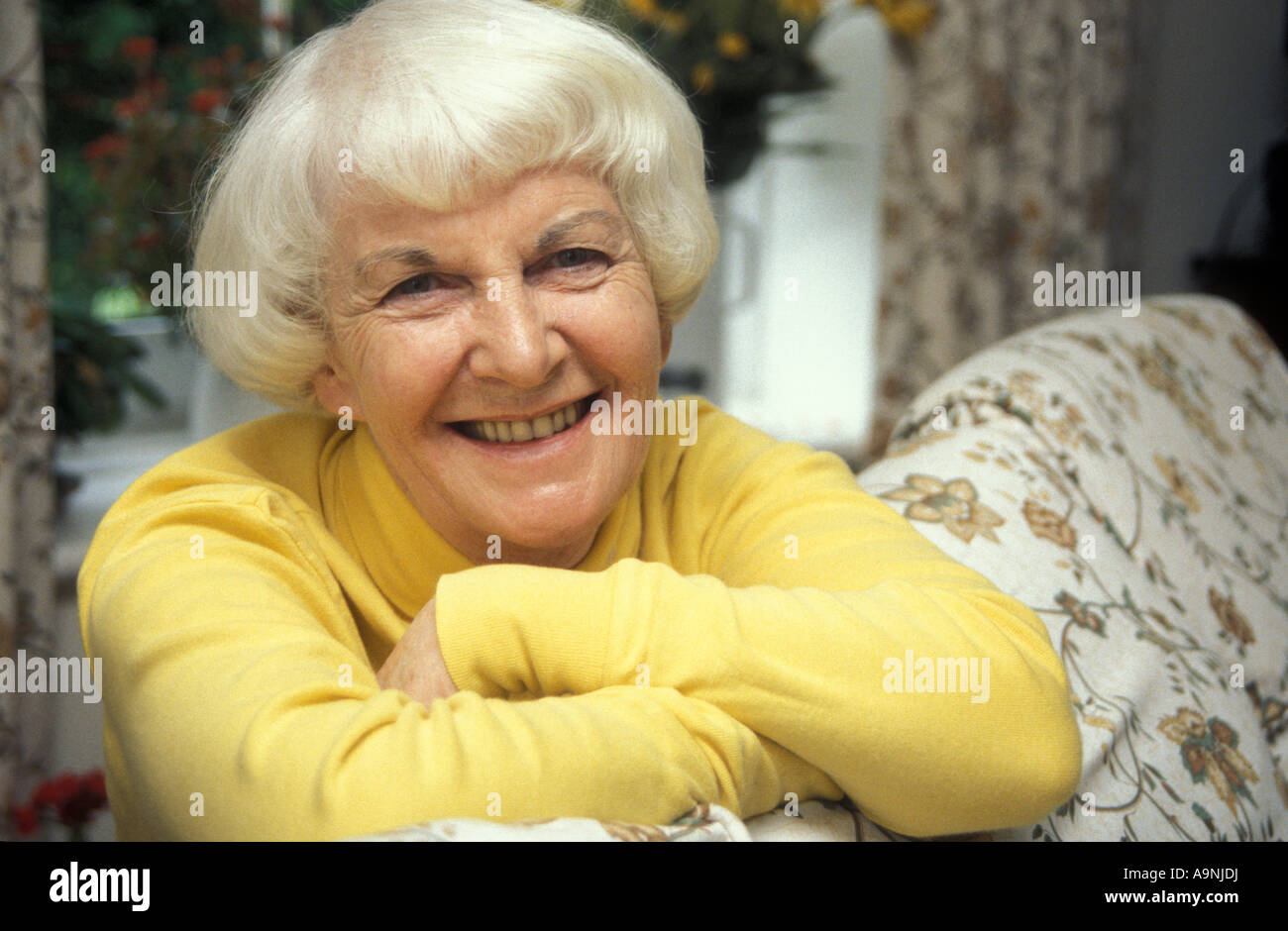 Ritratto felice dai capelli grigi donna matura sporgendoti posteriore del divano Foto Stock