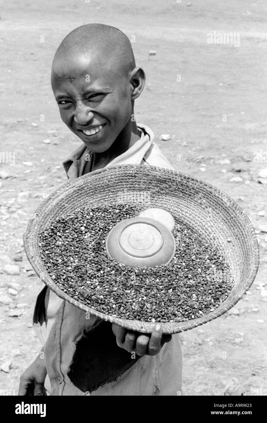 Ritratto B/N di un ragazzo allegro e sorridente che porta un cesto tessuto di legumi e grani da vendere per le strade di Adua. Tigray, Etiopia Foto Stock
