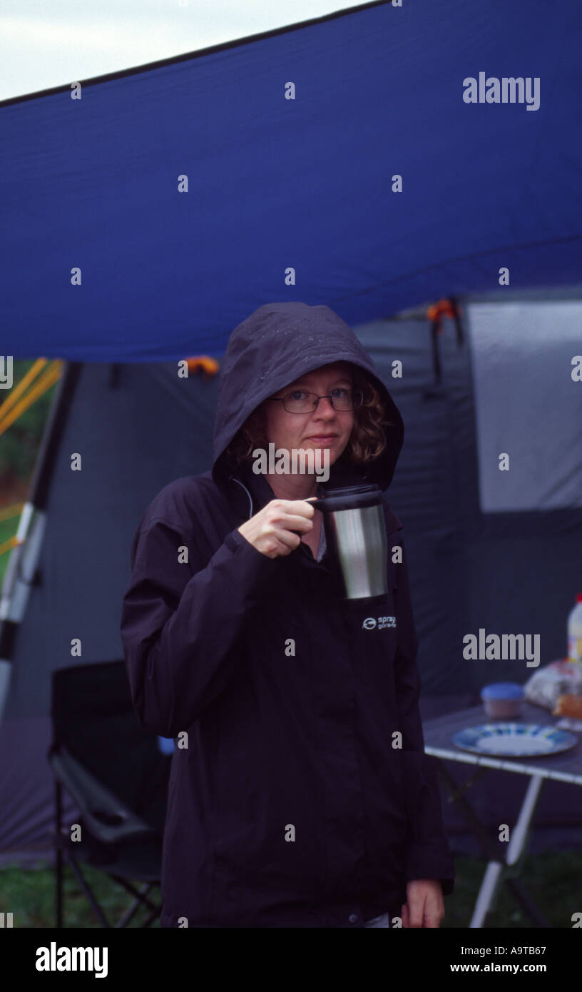 Persona in campeggio sotto la pioggia avente una tazza di tè Foto Stock