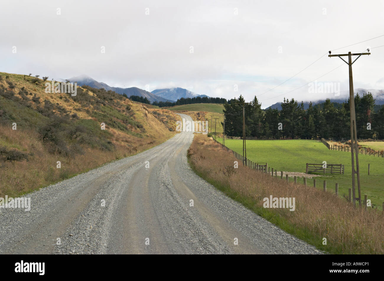 Nuova Zelanda Isola del Sud strada di ghiaia attraverso la zona rurale di Otago basso nuvole montagne in distanza di linee telefoniche Foto Stock