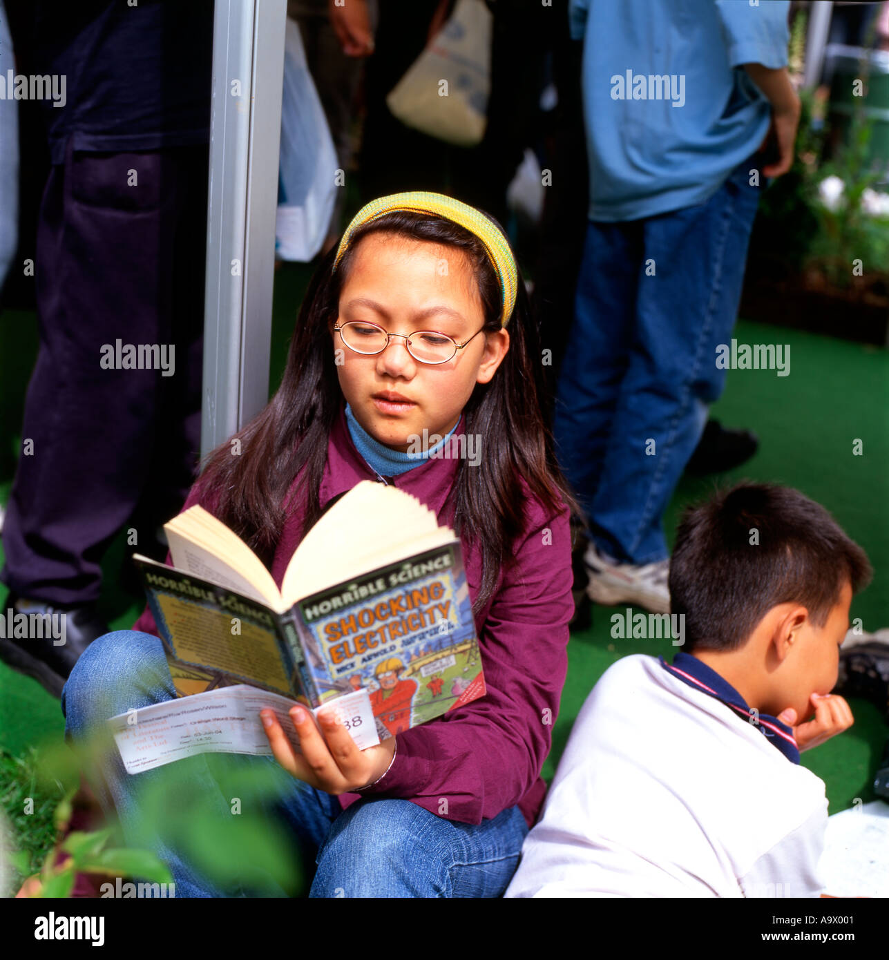 Una giovane ragazza cinese la lettura di un libro seduti in una coda presso il Festival di Fieno Hay-on-Wye Wales UK KATHY DEWITT Foto Stock