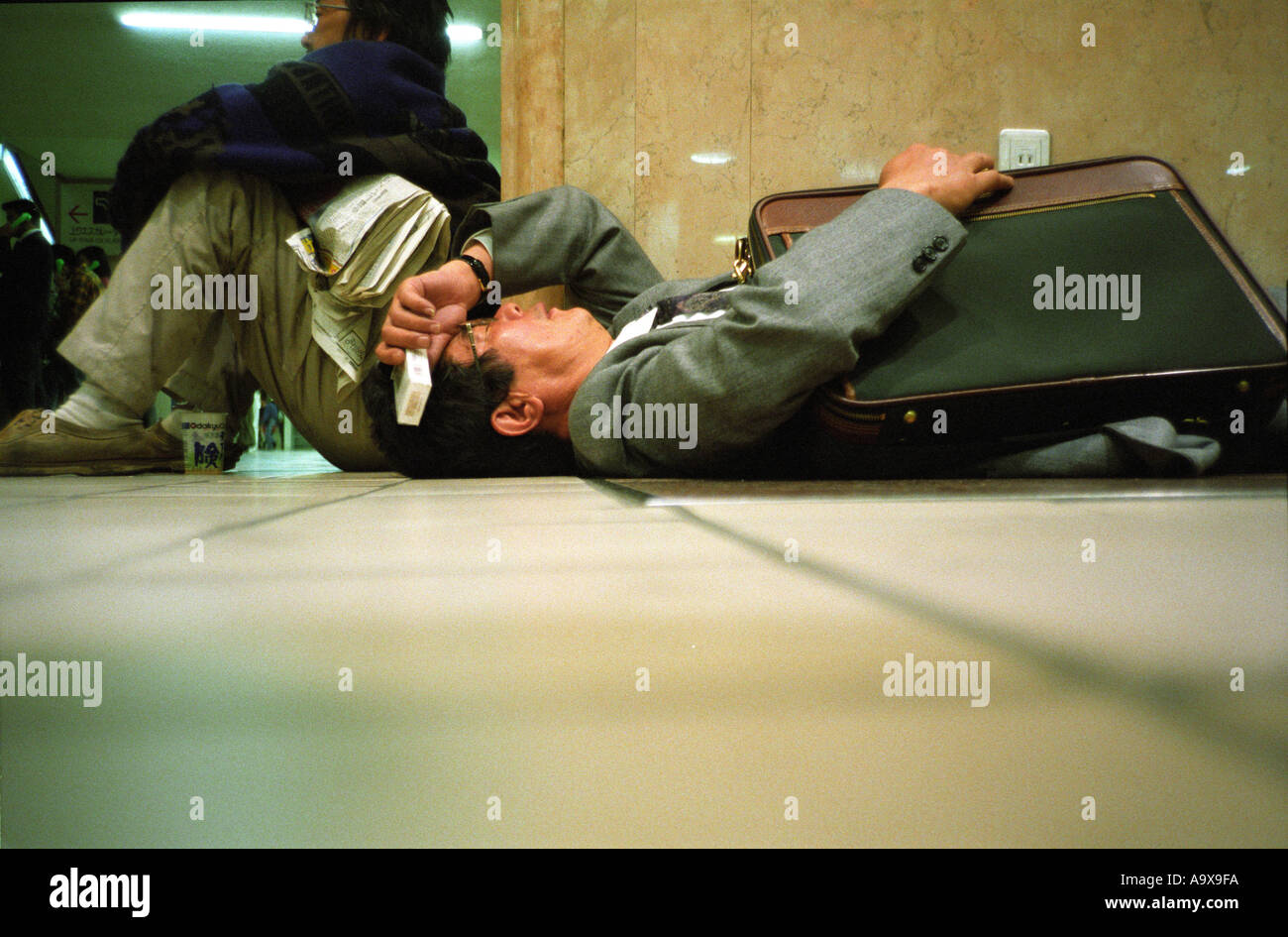 Un esaurito stipendio uomo si appoggia alla stazione di Shinjuku a Tokyo Foto Stock