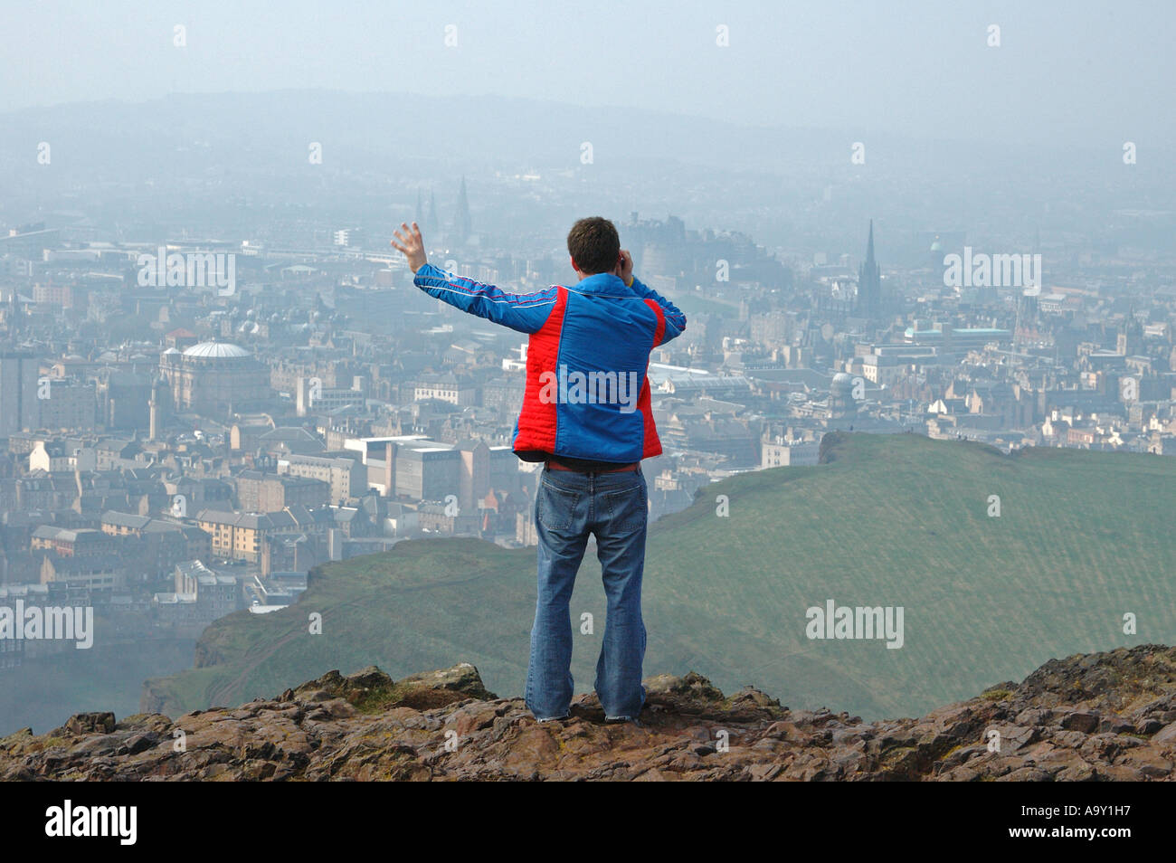 Un viandante colloqui su un telefono cellulare mentre guardando fuori alla vista di Edimburgo, Scozia, Regno Unito dalla sommità di Arthur Seat. Foto Stock