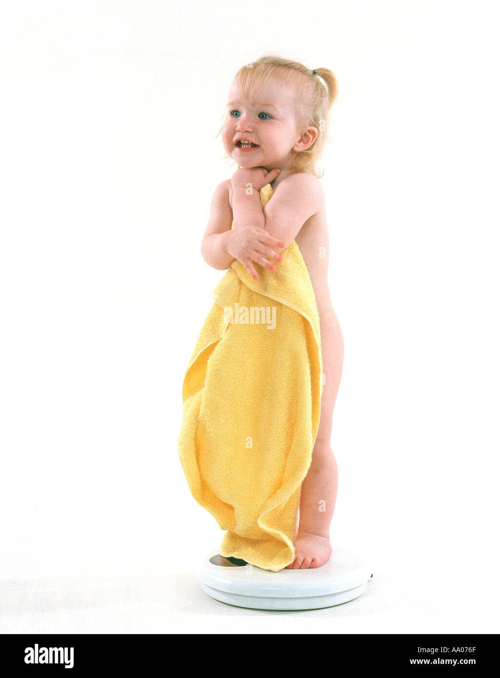 Baby girl permanente sulla bilancia da bagno con grande asciugamano giallo Foto Stock