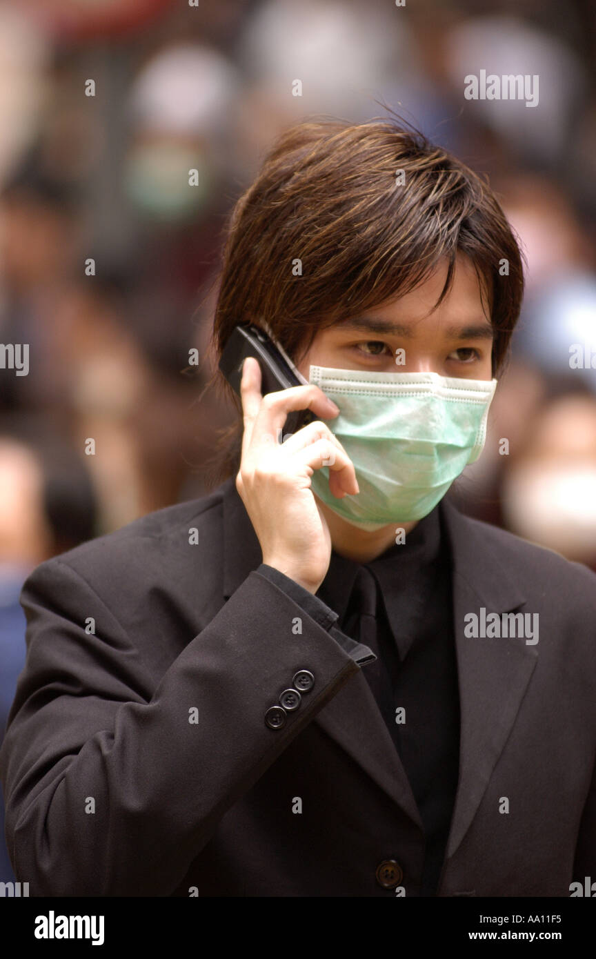 Un uomo con la maschera per il viso parlando sul suo telefono cellulare durante l'epidemia di SARS in Hong Kong 2003 Foto Stock