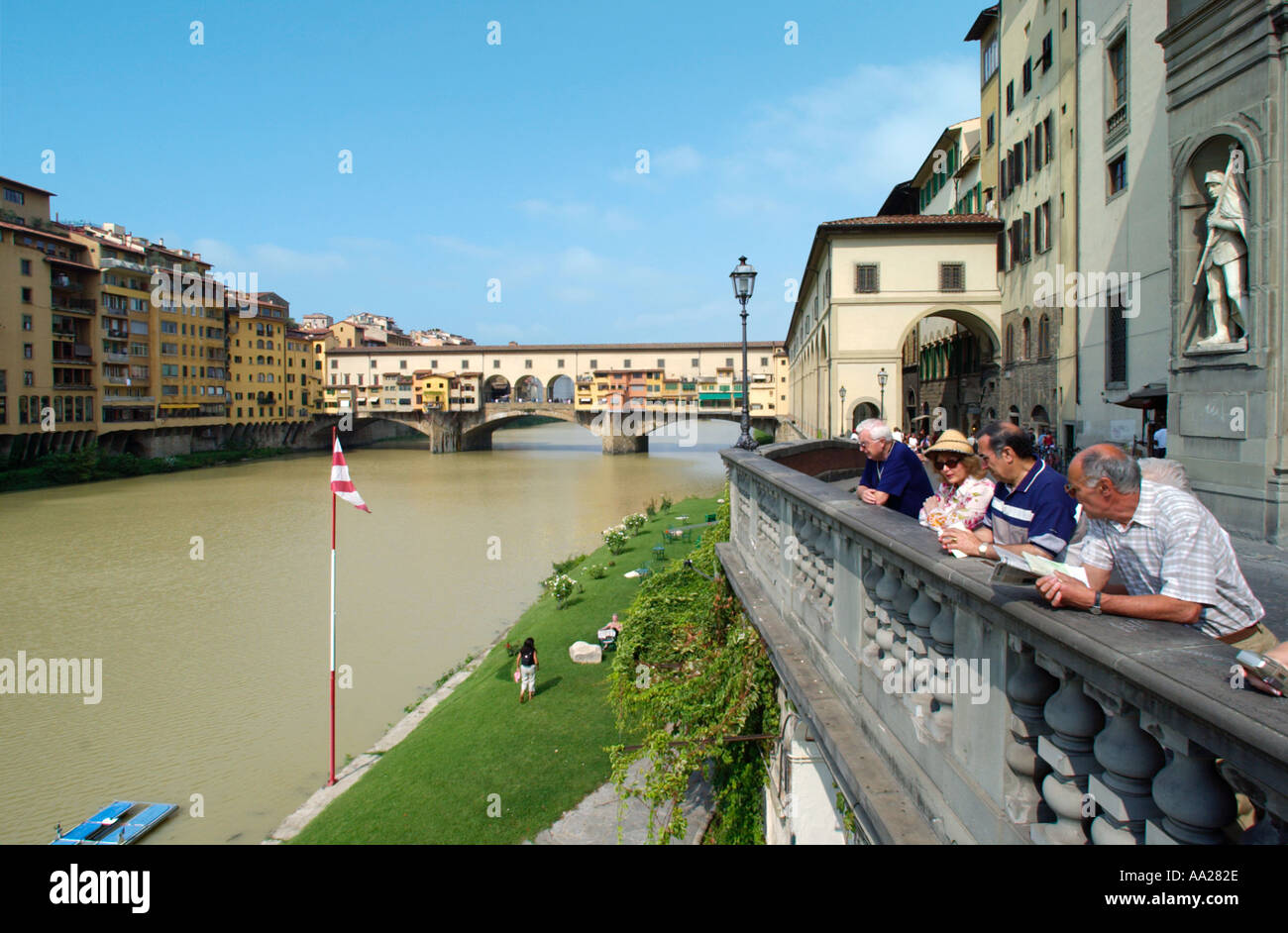 La gente appoggiata su un balcone accanto al fiume Arno con il Ponte Vecchio dietro, Firenze, Toscana, Italia Foto Stock