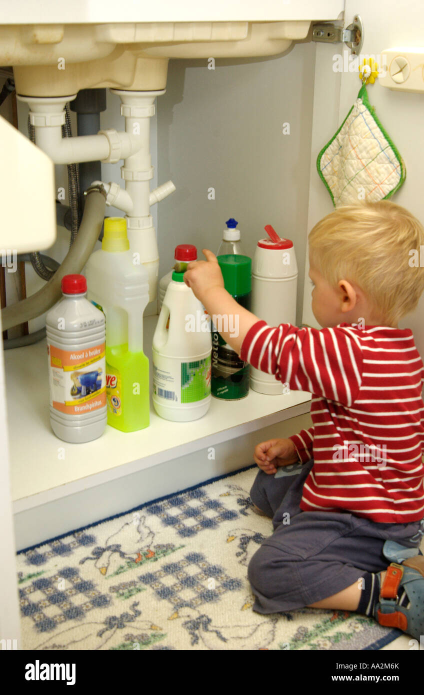 Bambino di raggiungere per flaconi di liquidi per la pulizia sotto il lavello in cucina - Pericolo / concetto di incidenti Foto Stock