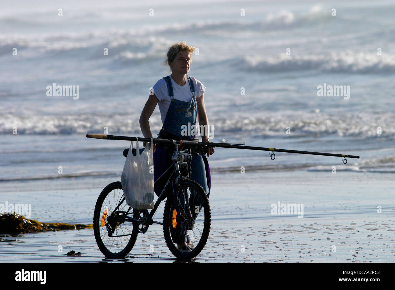 Signora passeggiando lungo la spiaggia con la sua mountain bike e canna da pesca Nuova Zelanda Foto Stock