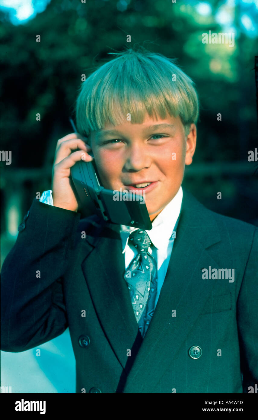 Giovane Biondo ragazzo che parla su un vecchio cellulare indossando un costume da lavoro fuori Grinning 'Looking at camera' 'vecchio cellulare » 1980s USA Foto Stock