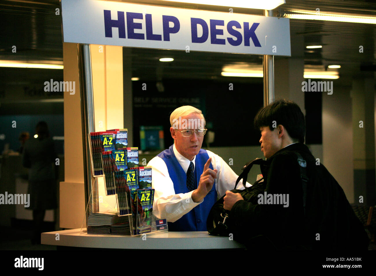 Un uomo anziano dà indicazioni per un giovane uomo asiatico presso un Help Desk presso il terminal dei voli interni in aeroporto di Auckland Nuova Zelanda Foto Stock