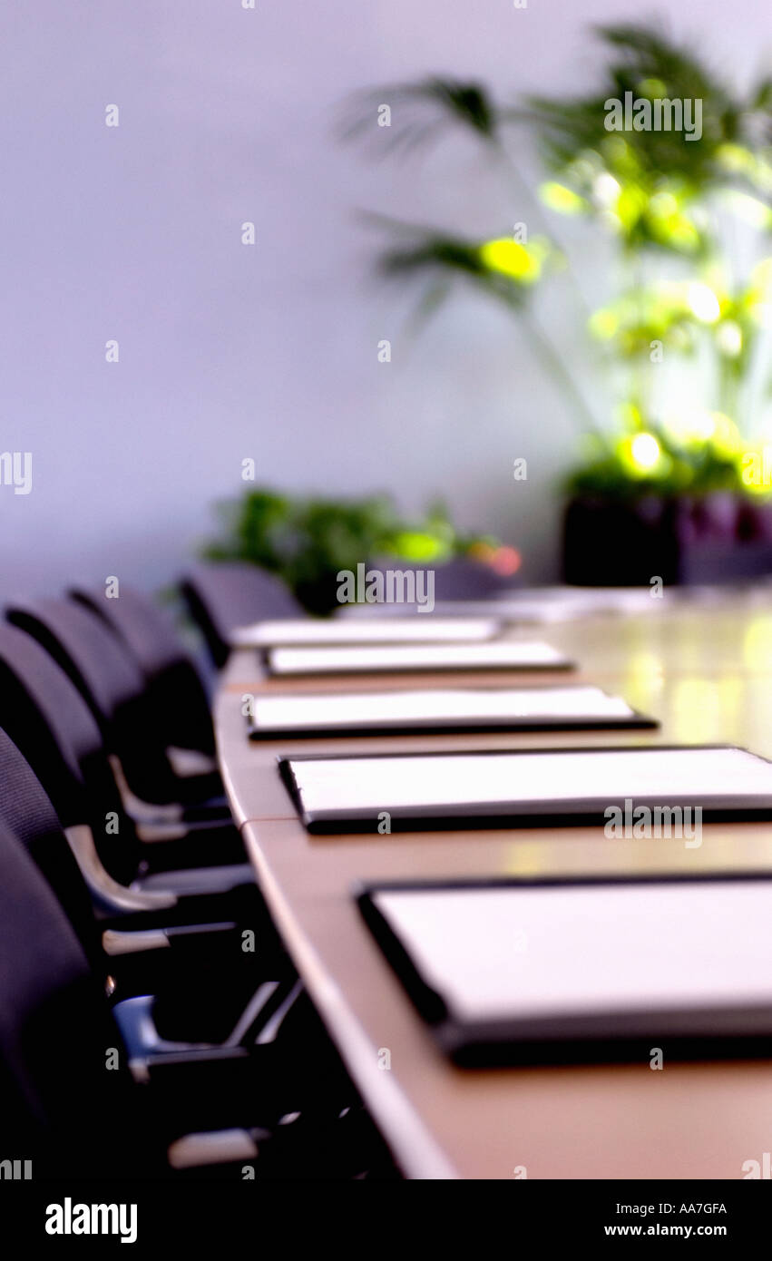 Sedie nere e blotter pad in pelle su un lungo tavolo in legno in una sala riunioni vuota Foto Stock