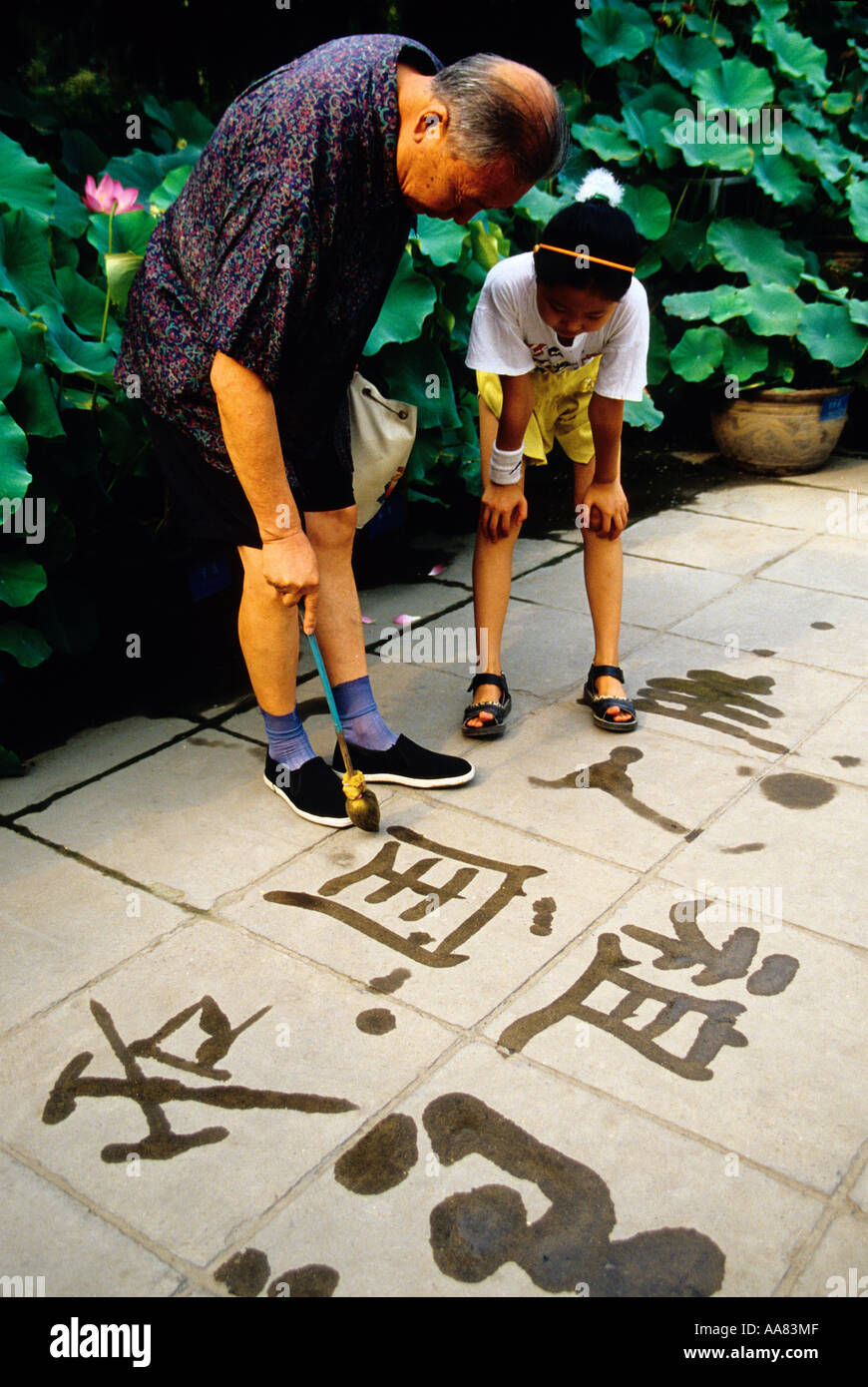 Pechino CINA Parco Jingshan nonno calligrafia di insegnamento al nipote con acqua pennello sul marciapiede in mattina presto Foto Stock
