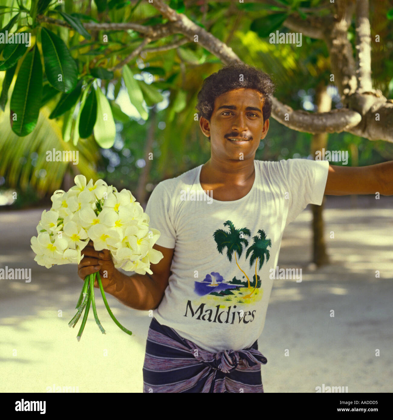 Giovani Maldivan sorridente uomo in bianco t-shirt holding mazzetto di fiori di frangipani su un isola Bandos alle Maldive Foto Stock