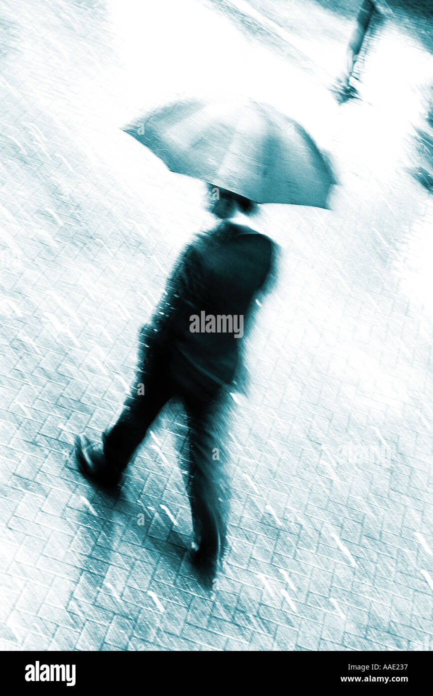 Un business man in tuta a piedi a velocità sotto un ombrello sotto la pioggia con movimento sfocate, Chester, Cheshire, Regno Unito Foto Stock