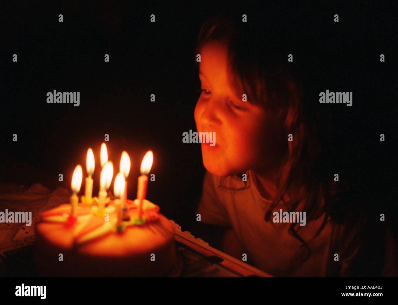 Piccola ragazza salta fuori il sette candele sulla sua torta di compleanno Foto Stock