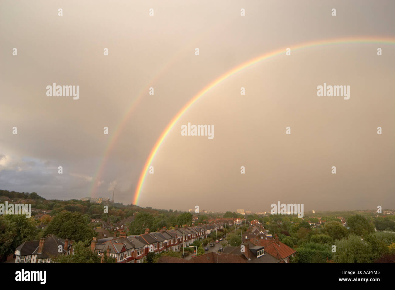 Lato sinistro della sera drammatico doppio arcobaleno nel cielo grigio al di sopra dei tetti di suburbana Foto Stock