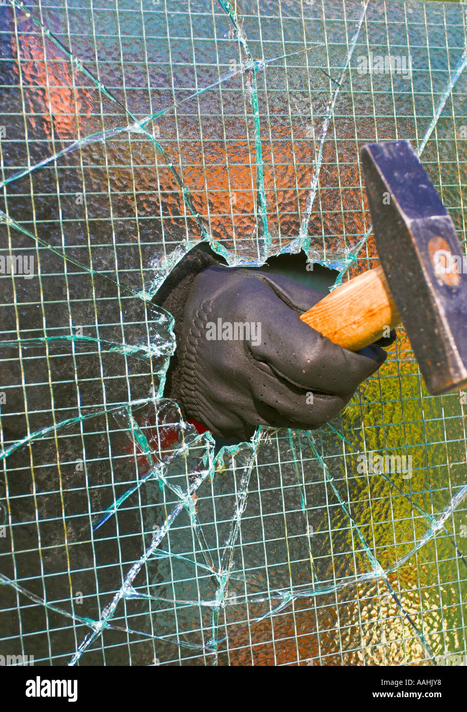 Ladro di rottura e di entrare in una proprietà privata da smashing attraverso il filo metallico applicato vetro utilizzando un martello. Foto Stock
