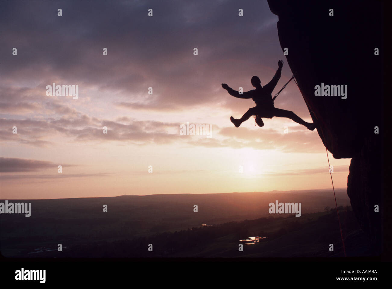 Rocciatore hanging off rocce al tramonto Foto Stock