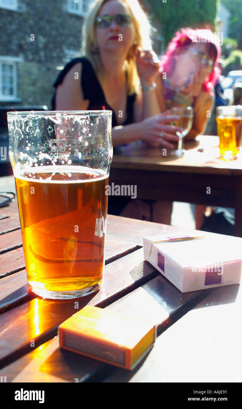 Birra e sigarette sul tavolo all'aperto presso il pub le ragazze in background Foto Stock