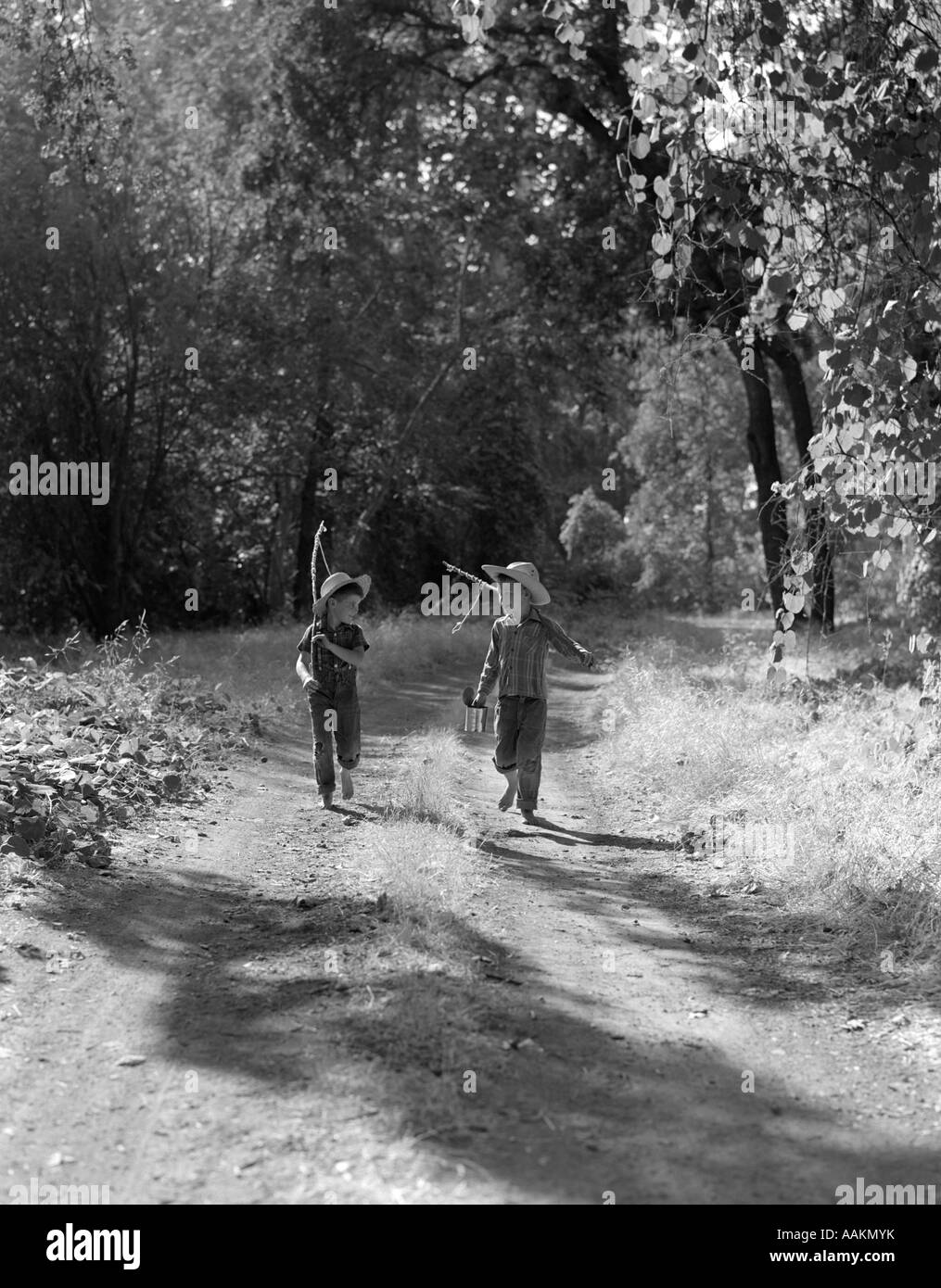 Negli anni quaranta anni cinquanta due ragazzi in salopette da PLAID camicie di cappelli di paglia camminare per strada sterrata porta pali pesca & possibile di esche Foto Stock