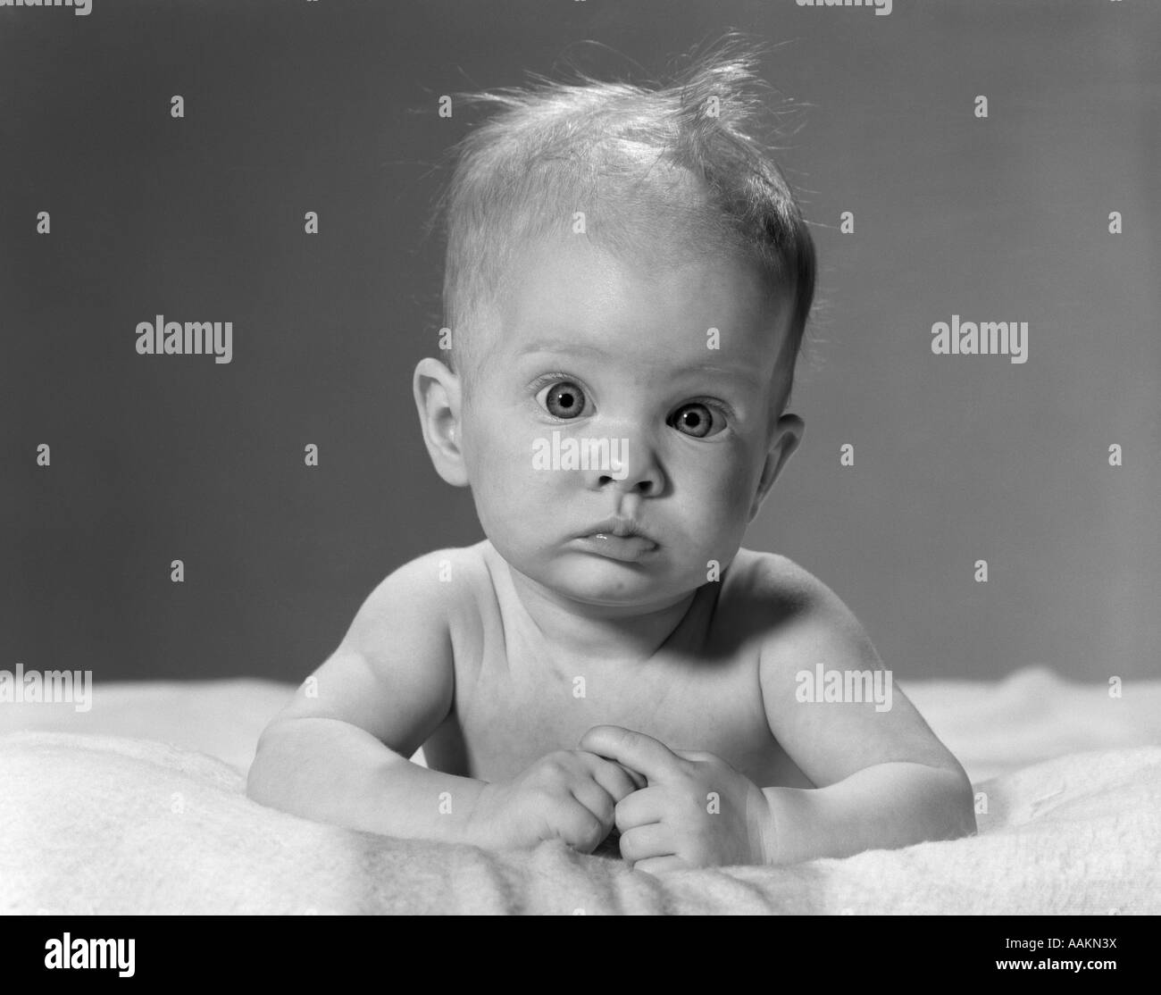 Anni sessanta ritratto Bambino giacente su stomaco disordinato con capelli e occhi sporgenti guardando la fotocamera Foto Stock